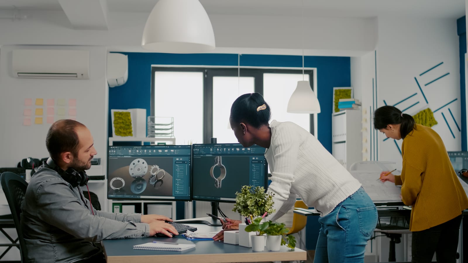 Engineers collaborating around dual monitors displaying 3D CAD gear models